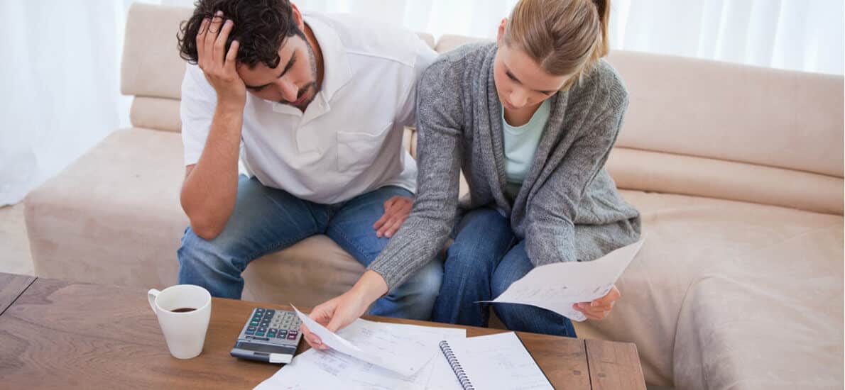 Homem e mulher preocupados olhando papéis sobre mesa com café e calculadora