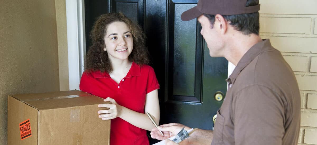 Mulher recebendo pacote na porta das mãos de homem que pede assinatura em uma prancheta